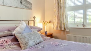 A bedroom with a bed, pillows, a nightstand, a vase with flowers, and a window with curtains. - 2 Bed in Westleton (oc-w42586) (Westleton)