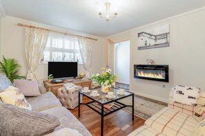 Ein Wohnzimmer mit Sofa, Sesseln, Couchtisch, Fernseher, Kamin und Dekoration.