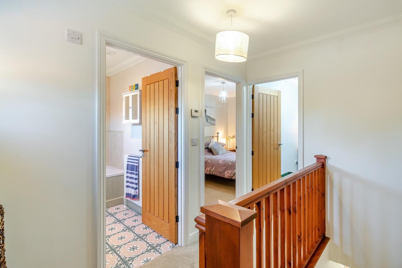 A hallway with a wooden door leading to a bedroom with a bed and a nightstand.