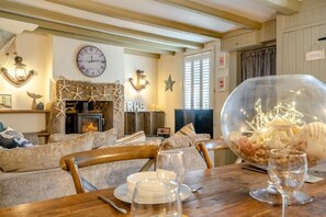 A cozy living room with a fireplace, a clock, and a dining table set for two. - 3 Bed in Robin Hoods Bay, Whitby (oc-g43284) (Robin Hood's Bay)