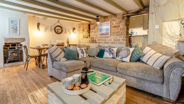 A cozy living room with a stone fireplace, a wooden dining table, and a comfortable sofa set. - 3 Bed in Robin Hoods Bay, Whitby (oc-g43284) (Robin Hood's Bay)