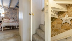 A bedroom with a bed, a staircase, and a stone wall with a star decoration. - 3 Bed in Robin Hoods Bay, Whitby (oc-g43284) (Robin Hood's Bay)