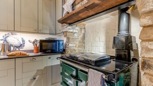 A kitchen with a stone wall, a microwave, a toaster, and a green oven. - 3 Bed in Robin Hoods Bay, Whitby (oc-g43284) (Robin Hood's Bay)