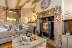 A cozy living room with a stone fireplace, a clock, and a wooden table with a mug and cookies. - 3 Bed in Robin Hoods Bay, Whitby (oc-g43284) (Robin Hood's Bay)