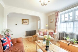 Una sala de estar acogedora con un sofá, una mesa con un jarrón y una taza, y una ventana con cortinas.