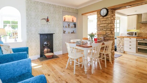 A cozy living room with a fireplace, a dining area with white chairs, and a kitchen with a stone wall and modern appliances. - 3 Bed in Waddington (oc-c45566) (Waddington)