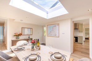 A dining area with a table set for four, a skylight above, a map on the wall, and a kitchen in the background. - 4 Bed in Bolingey (oc-m45595) (Bolingey)