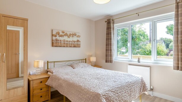 Een slaapkamer met een bed, nachtkastjes, een raam met gordijnen, een radiator en een schilderij aan de muur.