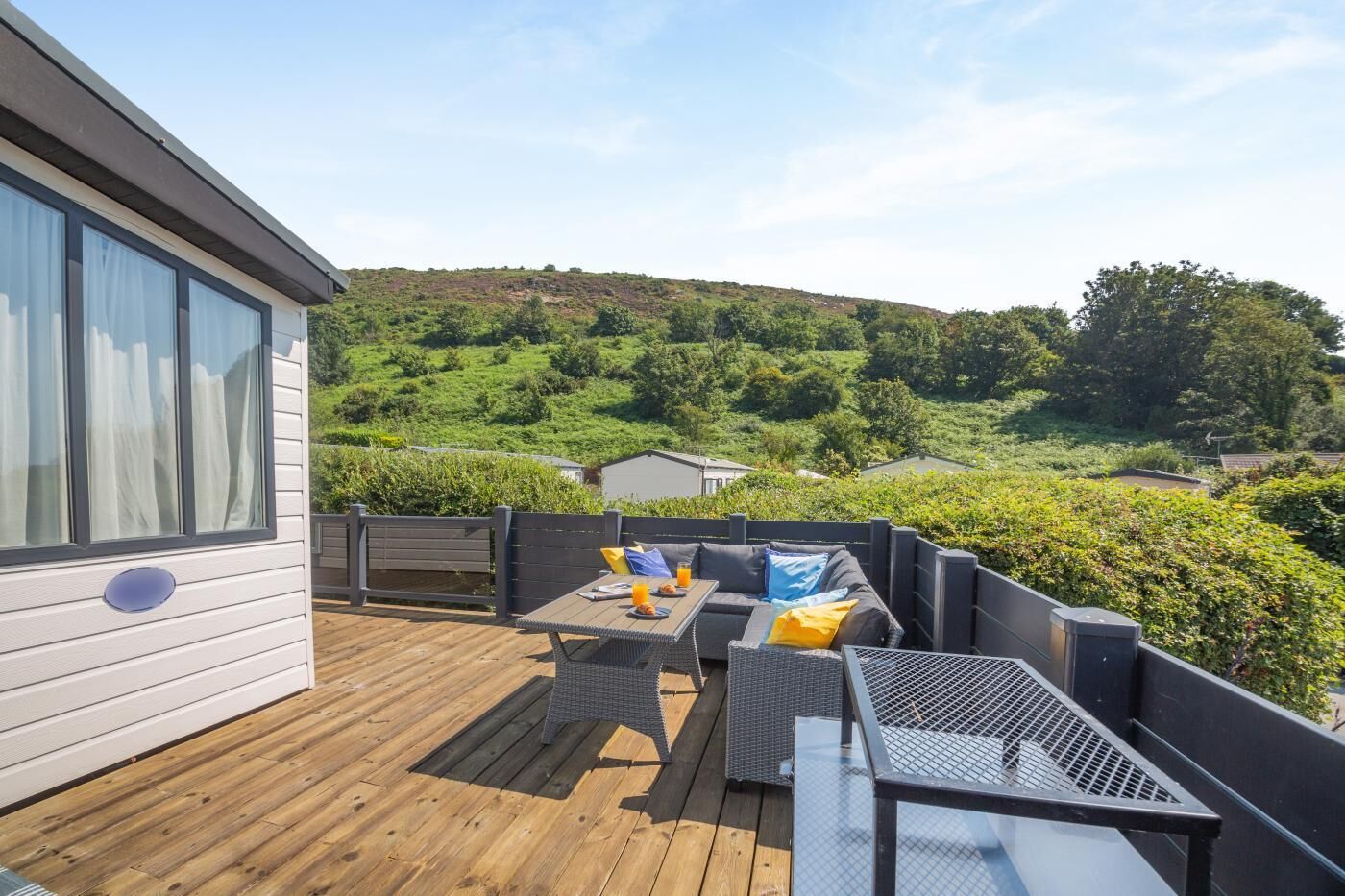 Une terrasse dotée de mobilier d’extérieur, offrant une vue sur un paysage vallonné, et un bâtiment avec de grandes fenêtres.