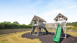 Un parque infantil con dos juegos de madera y un tobogán verde.
