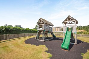 A playground with two wooden play structures and a green slide. - 3 Bed in Abersoch (oc-a45542) (Abersoch)