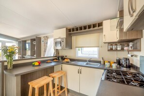 A compact kitchen with a microwave, toaster, sink, and stove. There are wooden stools and a vase with flowers on the counter.