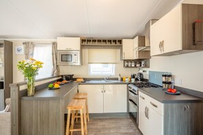 A compact kitchen with a microwave, stove, and sink. There are wooden stools and a small table with a vase of flowers.