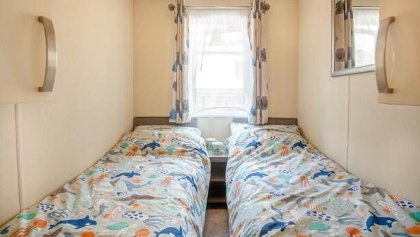 Una habitación pequeña con dos camas, cada una con una colcha de colores con motivos marinos.