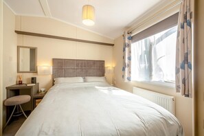 Ein Hotelzimmer mit einem großen Bett, einem Schreibtisch, einem Stuhl, einem Spiegel und einem Fenster mit Vorhängen.