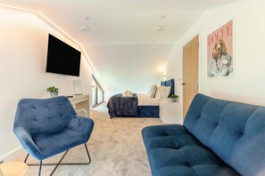 A modern bedroom with a bed, a blue armchair, a blue sofa, a flat-screen TV, and a poster on the wall. - 7 Bed in Broadwoodkelly (oc-b45447) (Broadwood Kelly)