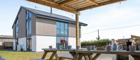 A modern two-story building with large windows and a covered outdoor area with picnic tables.