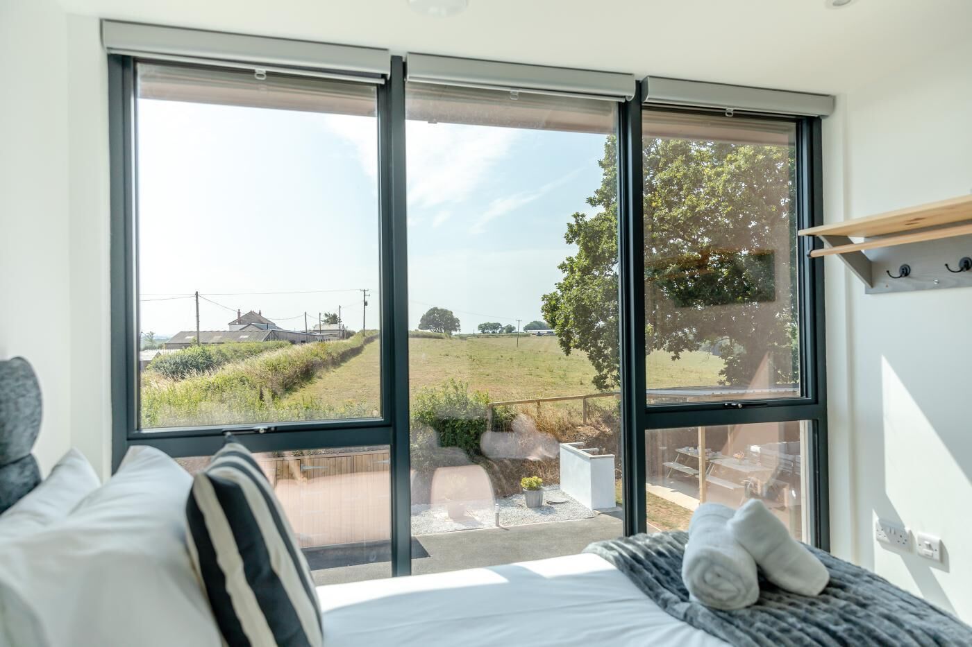A bedroom with a large window, a bed, and a view of a rural landscape.