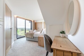 A modern bedroom with a bed, a desk, a chair, a large mirror, and a view of greenery through a sliding door. - 7 Bed in Broadwoodkelly (oc-b45447) (Broadwood Kelly)