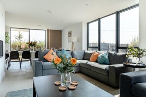 A modern living room with a grey sofa, a dining table with chairs, and large windows. - 7 Bed in Broadwoodkelly (oc-b45447) (Broadwood Kelly)