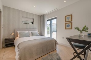 Ein modernes Schlafzimmer mit einem großen Bett, Nachttischen, einem Schreibtisch und Blick durch ein Fenster.