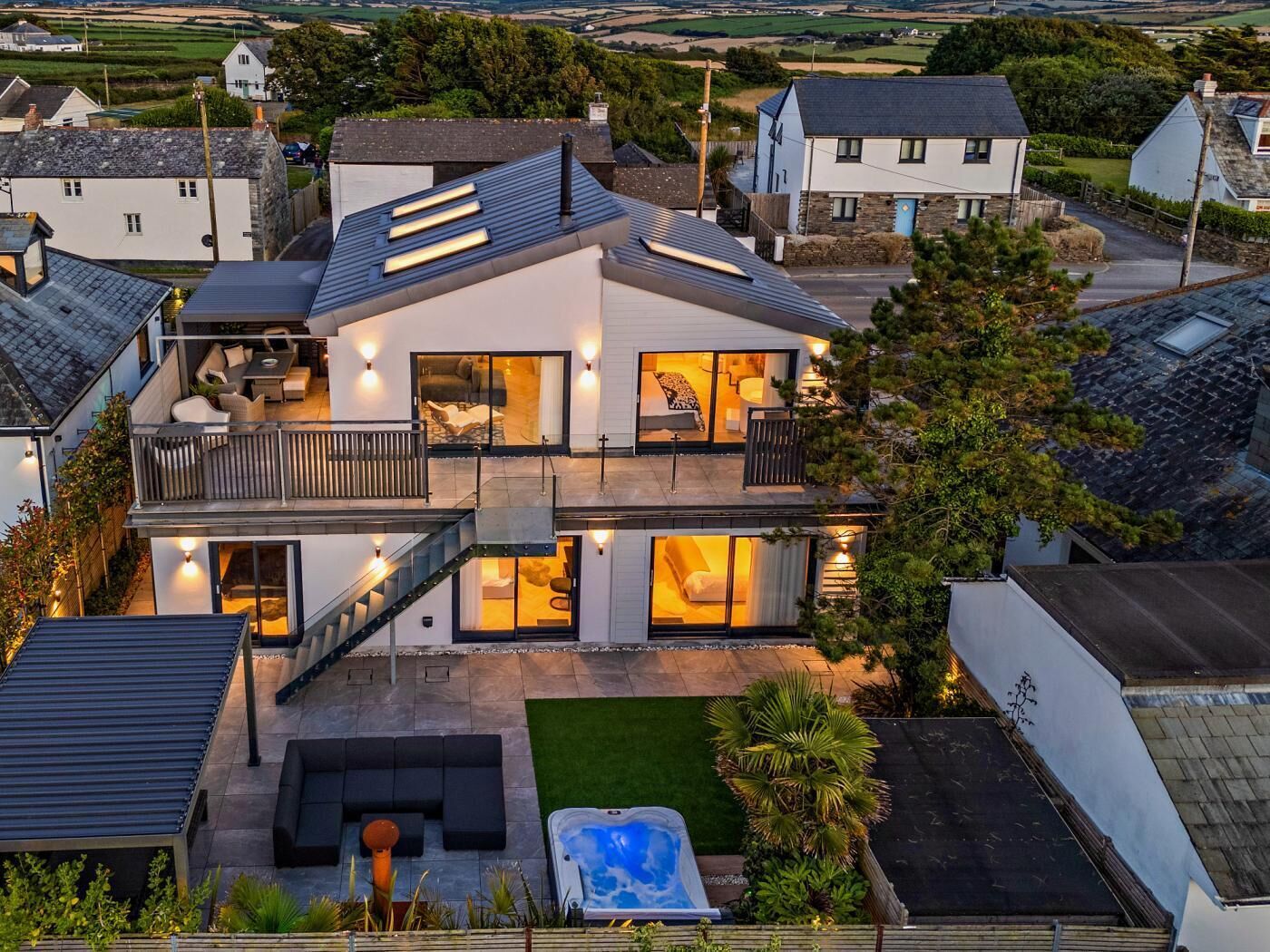 A modern two-story house with a patio, a hot tub, and a view of the surrounding countryside.