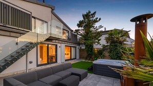 Et moderne hus med en glastrappe, en terrasse med sofa og et spabad.