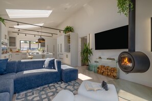 Ein modernes Wohnzimmer mit einer Eckcouch, einem Kamin, einem Flachbildfernseher und einer Küche im Hintergrund.