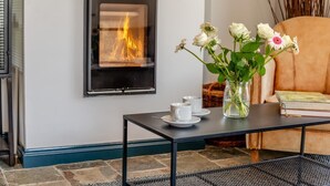 A fireplace with visible flames, a table with cups and a vase of flowers, and a leather chair. - 5 Bed in Windmill (oc-o45436) (Trevone)