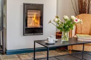 Ein Kamin mit sichtbaren Flammen, ein Tisch mit Tassen und eine Blumenvase sowie ein Ledersessel.