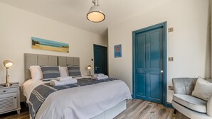 A hotel room with a bed, bedside lamps, a blue door, a gray sofa, and artwork on the walls. - 5 Bed in Windmill (oc-o45436) (Trevone)