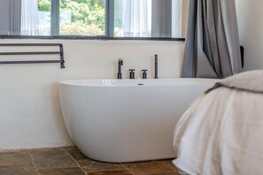 Een moderne badkamer met een vrijstaand bad, een handdoekrek en een raam met gordijnen.