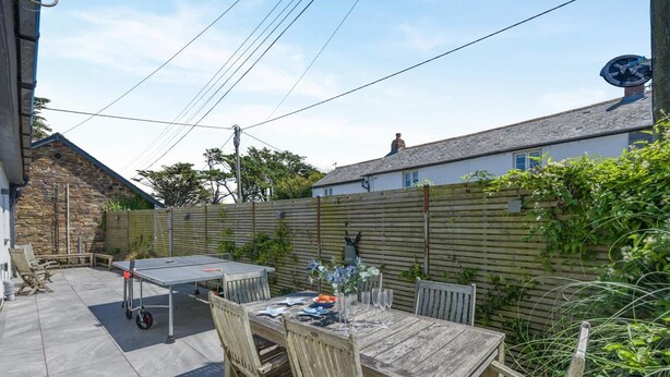 A patio area with a table set for dining, surrounded by a wooden fence and a stone wall. - 5 Bed in Windmill (oc-o45436) (Trevone)