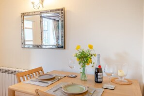 A dining table set with plates, cutlery, a vase with flowers, a bottle of wine, and glasses. - 2 Bed in Castle Acre (oc-r18323) (Castle Acre)