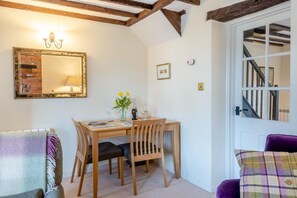 A dining area with a wooden table, chairs, and a vase with flowers. There is a mirror on the wall and a staircase in the background. - 2 Bed in Castle Acre (oc-r18323) (Castle Acre)