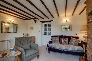 A cozy living room with a wooden ceiling, a purple sofa, a grey armchair, and a small table with a cake. - 2 Bed in Castle Acre (oc-r18323) (Castle Acre)