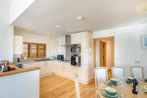 A modern kitchen with white cabinets, a wooden dining table set with green plates, and a built-in oven. - 3 Bed in Marshwood (oc-w34352) (Marshwood)
