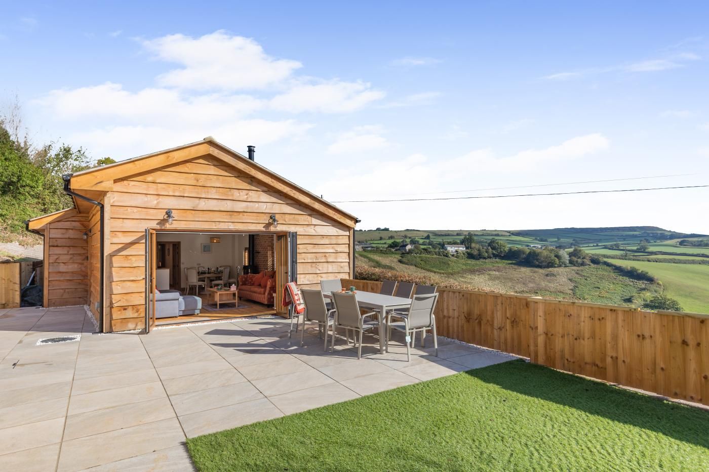 A wooden cabin with a patio, a dining area, and a view of the countryside.