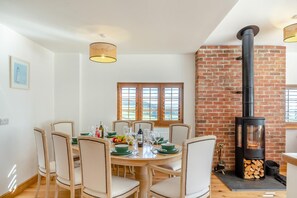 A dining area with a brick wall, a wood-burning stove, and a table set for four. - 3 Bed in Marshwood (oc-w34352) (Marshwood)