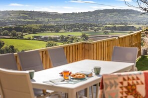 A dining area with a table and chairs, overlooking a scenic landscape with hills and fields. - 3 Bed in Marshwood (oc-w34352) (Marshwood)