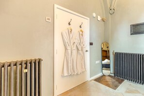 A hallway with a radiator, a door with two robes hanging, and a mirror reflecting a room. - 2 Bed in Market Stainton (oc-s45536) (Market Stainton)