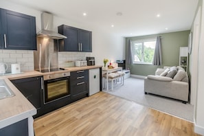 A compact kitchen with modern appliances, a dining area with a table and chairs, and a living room with a sofa. - 1 Bed in Chacewater (oc-l45269) (Chacewater)