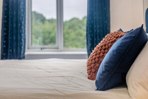 A bed with a white mattress and blue and brown pillows, a window with a view of greenery, and blue curtains. - 1 Bed in Chacewater (oc-l45269) (Chacewater)