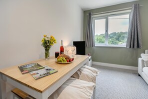 Ein Hotelzimmer mit einem Holztisch, einer Blumenvase, einer Weinflasche, einem Obstteller und einer Zeitschrift.