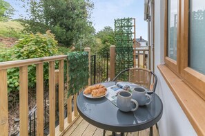 A balcony with a table set for two, featuring croissants and two mugs. - 1 Bed in Chacewater (oc-l45269) (Chacewater)