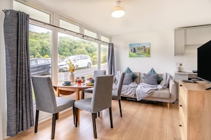A modern living room with a sofa, chairs, a dining table, and a TV.