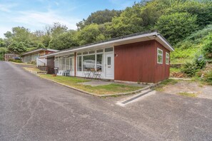 A single-story building with a red exterior, a covered patio area with seating, and a paved driveway. - 2 Bed in Caswell Bay (oc-s45738) (Newton)