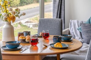 A dining area with a table set for two, featuring a vase of flowers, a bottle, croissants, and glasses of red beverage. - 2 Bed in Caswell Bay (oc-s45738) (Newton)
