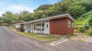 A single-story building with a red exterior, a covered patio area with seating, and a paved driveway. - 2 Bed in Caswell Bay (oc-s45738) (Newton)
