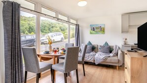A modern living room with a sofa, chairs, a dining table, and a TV. - 2 Bed in Caswell Bay (oc-s45738) (Newton)